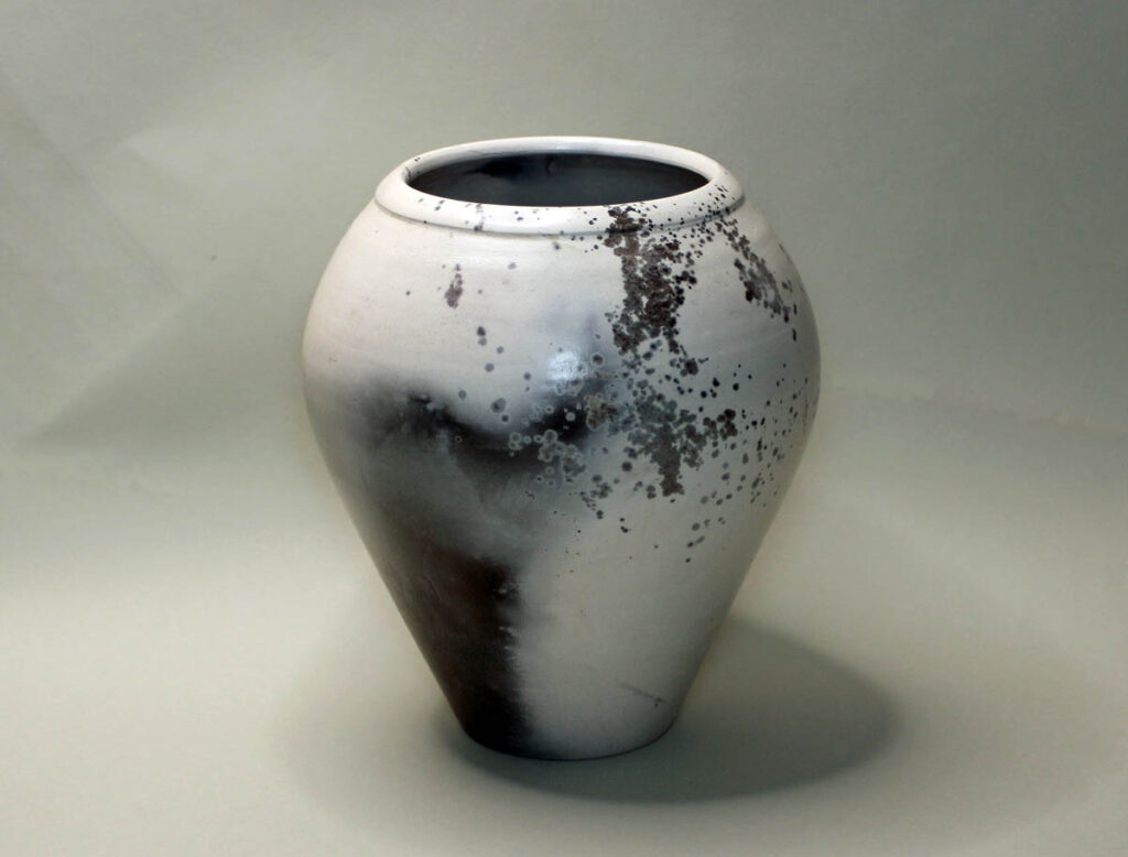 A white vase with black and brown paint on it.